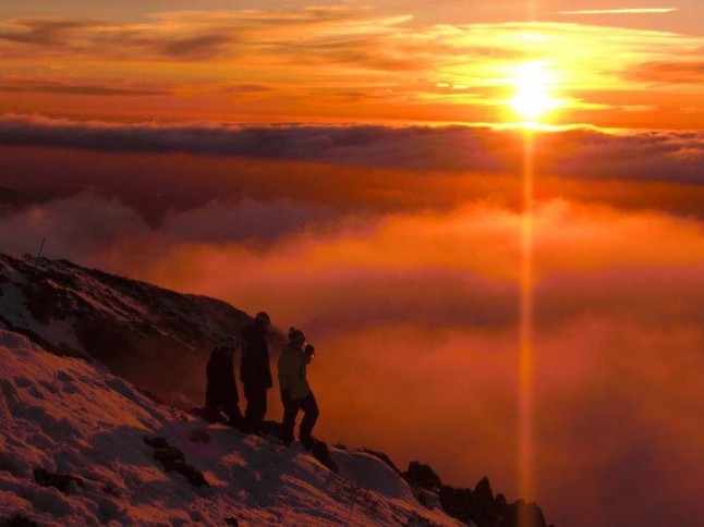 three skiers watching the sunset atop a mountain